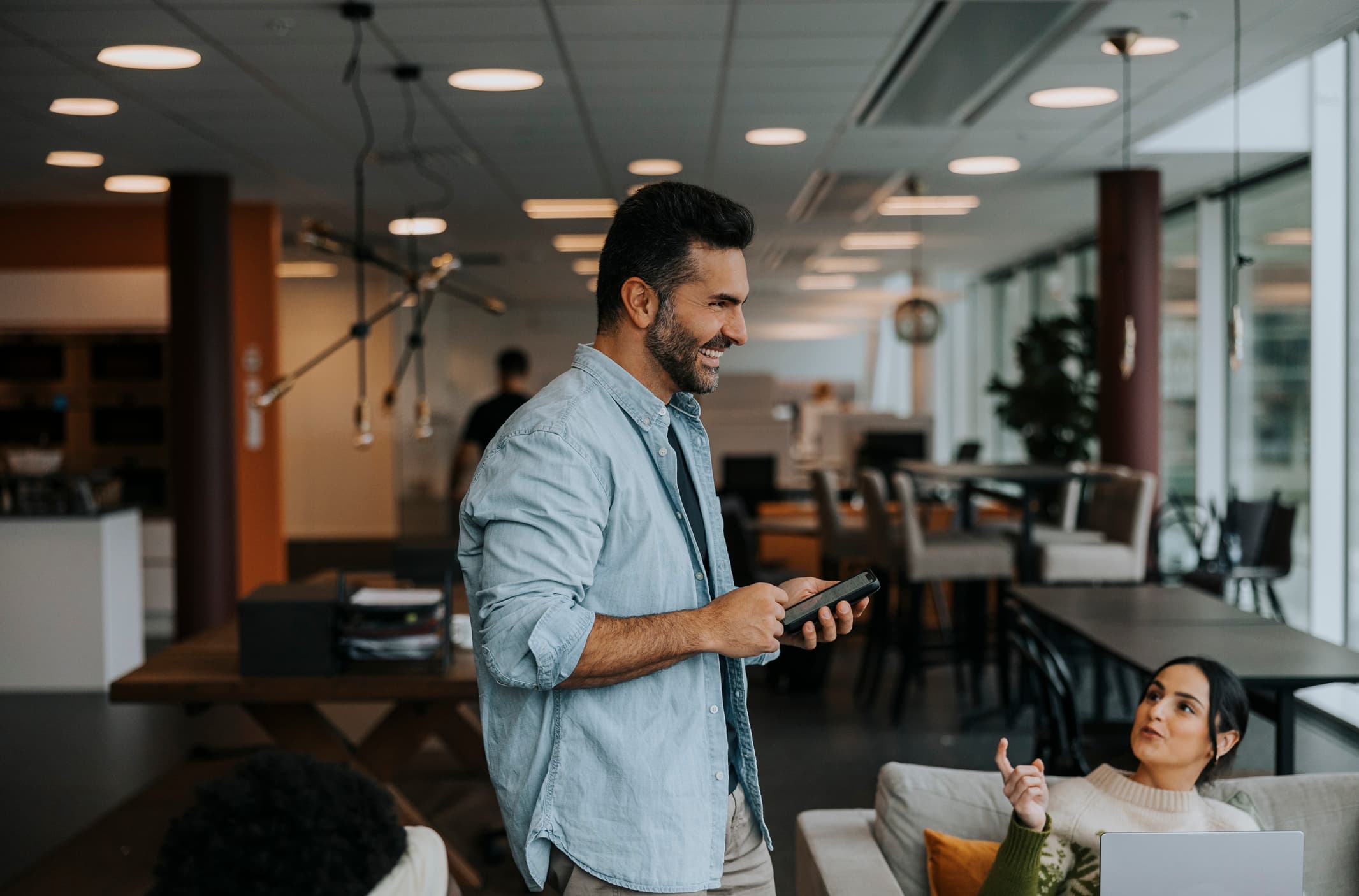 Side view of happy mature businessman standing with smart phone by female colleague during meeting